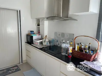 Modern kitchen with sleek cabinets and black countertop, featuring a range hood and organized appliances.