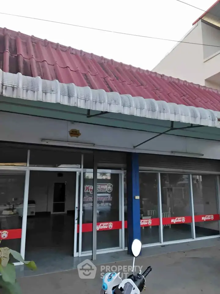 Commercial property with glass storefront and red roof, ideal for retail or office space.