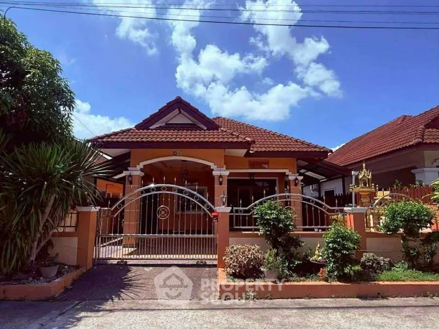 Charming single-story house with gated entrance and lush garden under a clear blue sky.