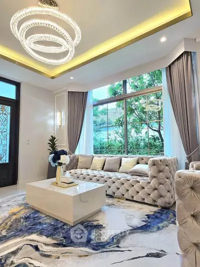 Luxurious living room with elegant chandelier and plush sofa, featuring large windows and stylish decor.