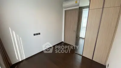 Modern bedroom with wooden flooring and built-in wardrobe, featuring natural light from a large window.