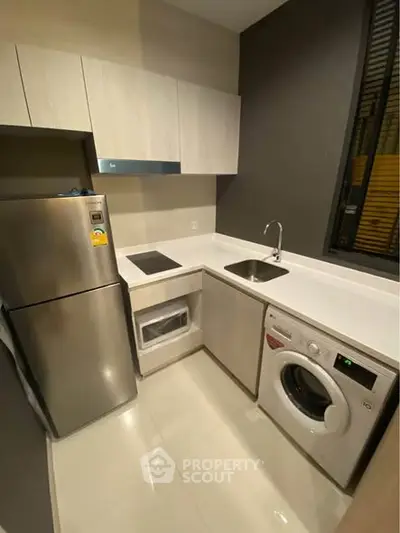 Modern kitchen with sleek appliances and efficient layout, featuring a washing machine and fridge.