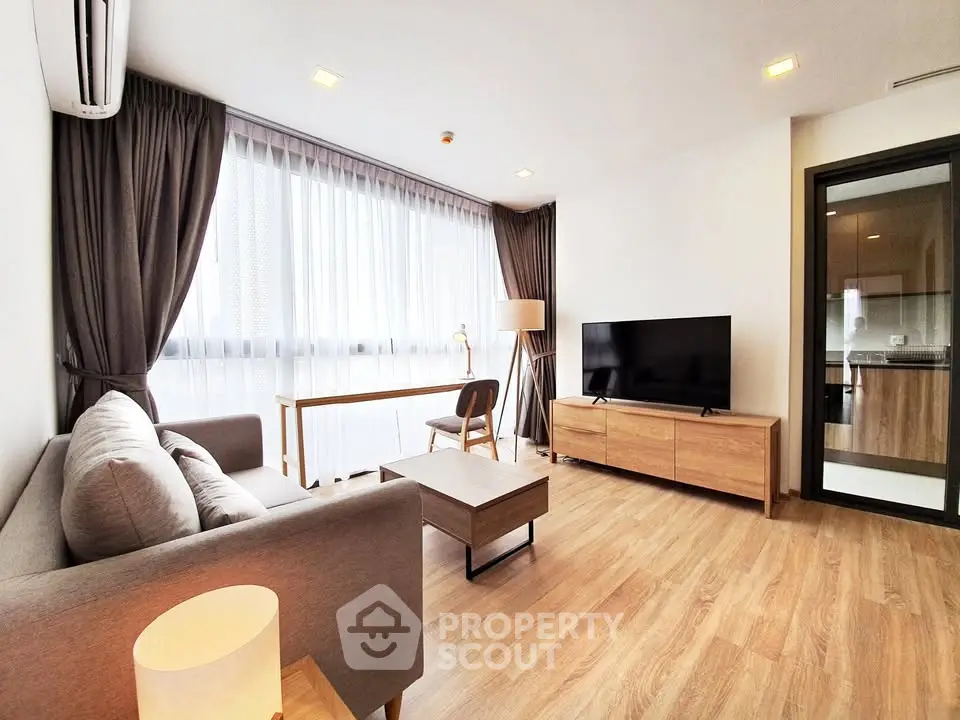 Modern living room with wooden flooring, large window, and stylish furniture in a cozy apartment.
