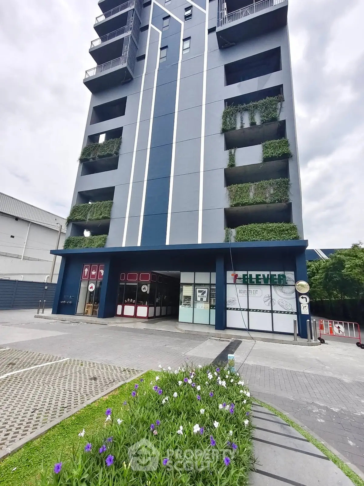 Modern apartment building with lush green balconies and vibrant flower garden.