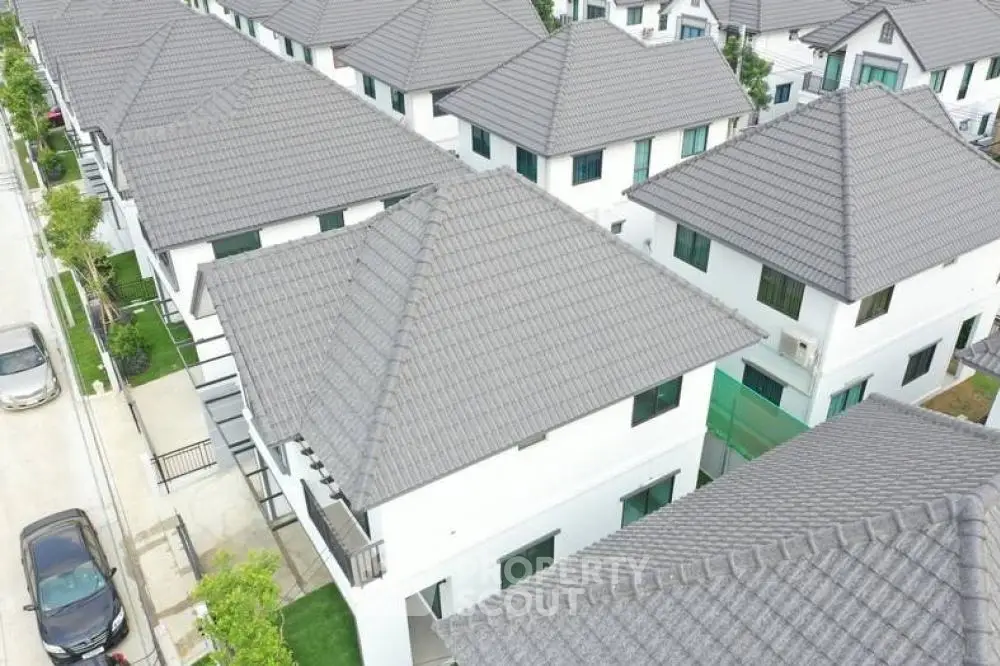 Aerial view of a modern residential development featuring rows of pristine white houses with grey tiled roofs, showcasing a uniform and well-planned suburban neighborhood.