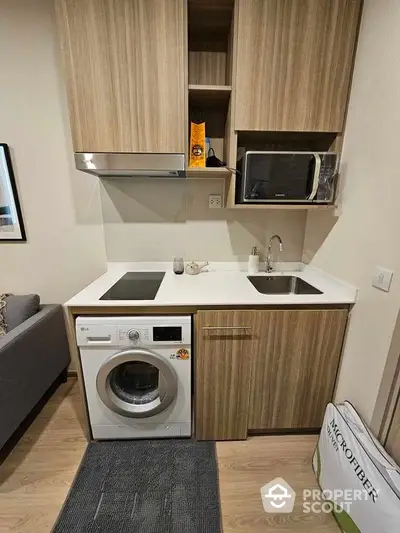 Modern compact kitchen with washing machine and microwave in stylish apartment.