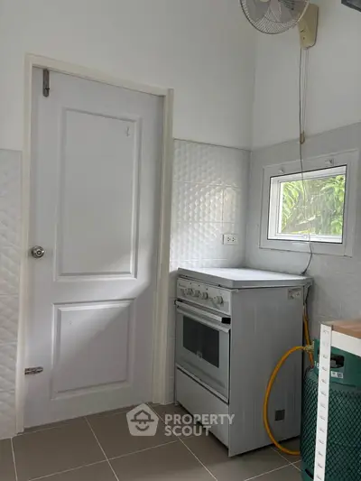 Compact kitchen with gas stove and window, featuring modern white tiles and neutral tones.