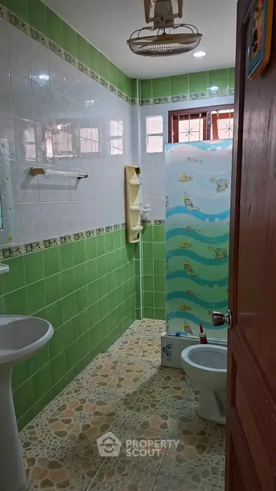 Charming bathroom with green tiles and playful shower curtain in cozy home.