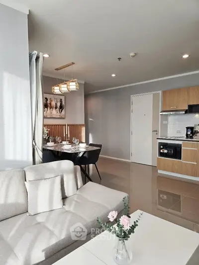 Modern open layout living room with stylish kitchen and dining area, featuring elegant decor and natural light.