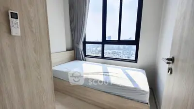 Cozy bedroom with large window offering stunning city views, perfect for urban living.