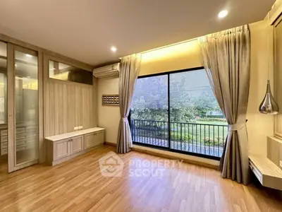 Spacious living room with large window and garden view, featuring elegant wood flooring and modern lighting.