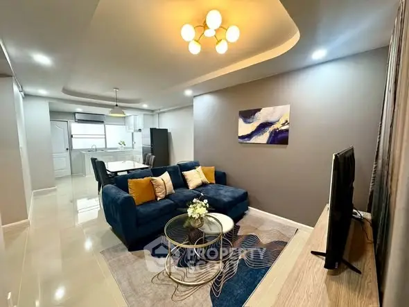 Modern living room with stylish decor and open kitchen layout, featuring a cozy blue sofa and elegant lighting.