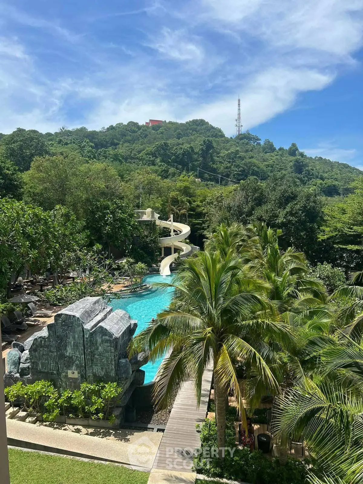 Luxurious resort pool with water slide and lush greenery, perfect for tropical relaxation.