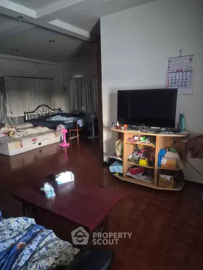 Spacious living area with TV, bed, and wooden flooring, ideal for cozy living.