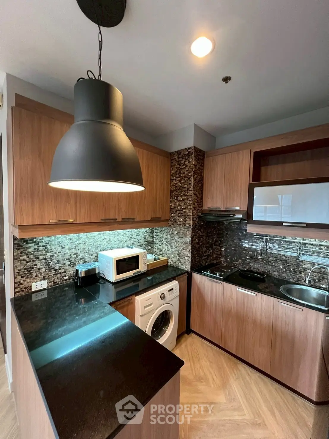 Modern kitchen with sleek wooden cabinets, black countertops, and built-in appliances including a washing machine.