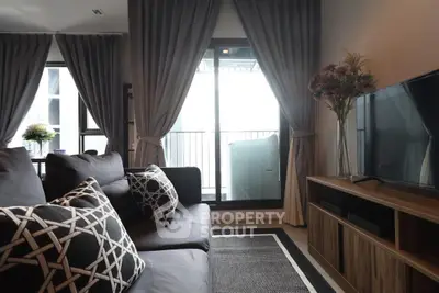 Modern living room with stylish sofa, large TV, and elegant curtains leading to a balcony.
