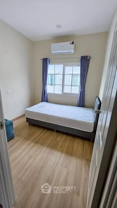 Cozy bedroom with wooden flooring and natural light, featuring a single bed and air conditioning.