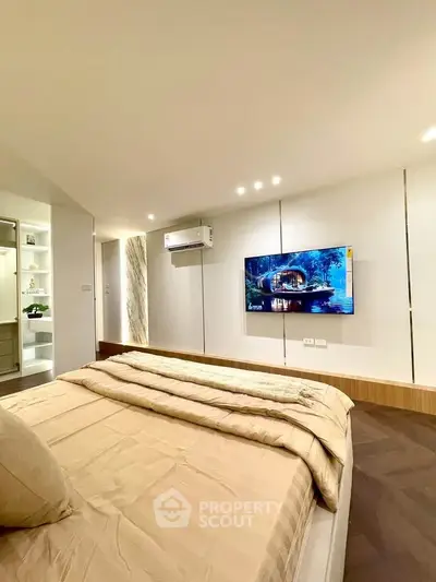 Modern bedroom with wall-mounted TV and air conditioning, featuring elegant lighting and cozy bedding.