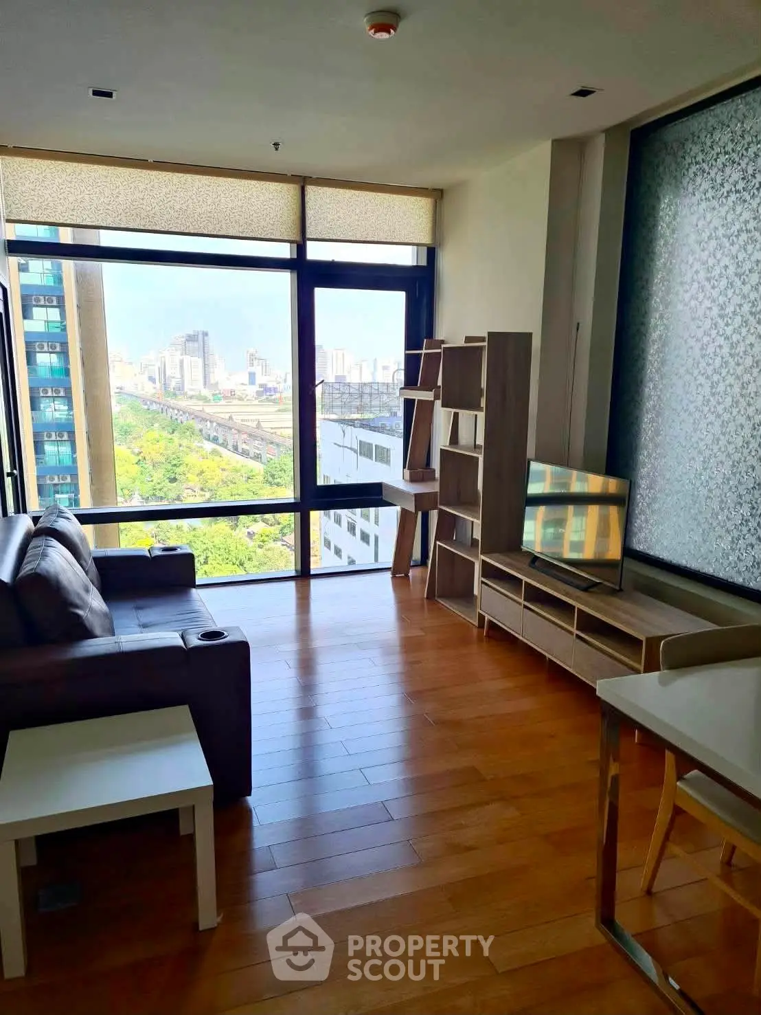 Modern living room with large window offering city view, stylish furniture, and wooden flooring.