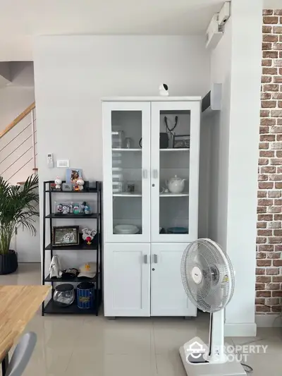 Modern interior with white cabinet, fan, and decorative shelves in a stylish living space.