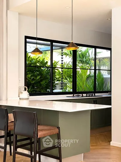 Modern kitchen with open layout, featuring sleek countertops and large windows overlooking lush greenery.
