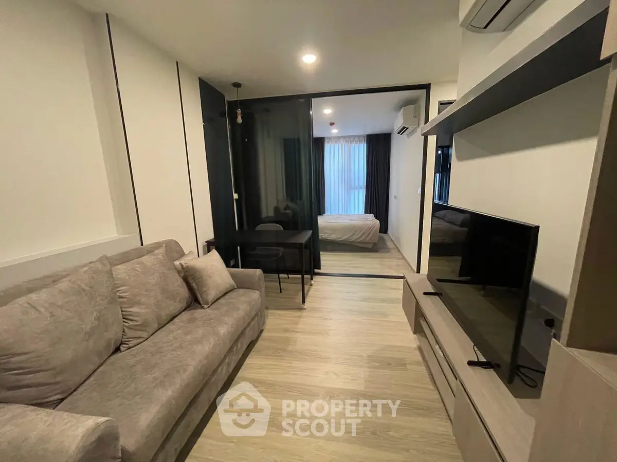 Modern living room with cozy sofa and TV, open view to bedroom, stylish interior design.