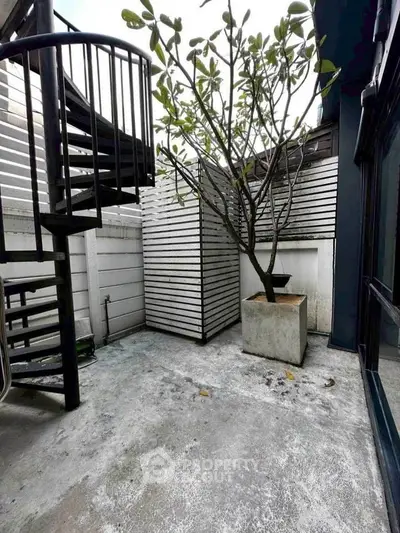 Charming outdoor patio with spiral staircase and potted tree, perfect for relaxation.