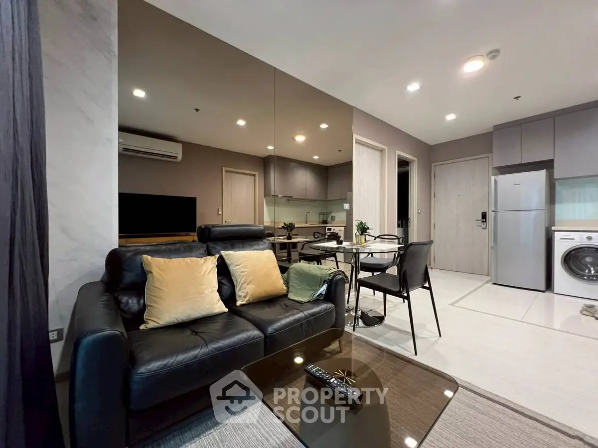 Modern living room with sleek black leather sofa, glass coffee table, and open kitchen layout.