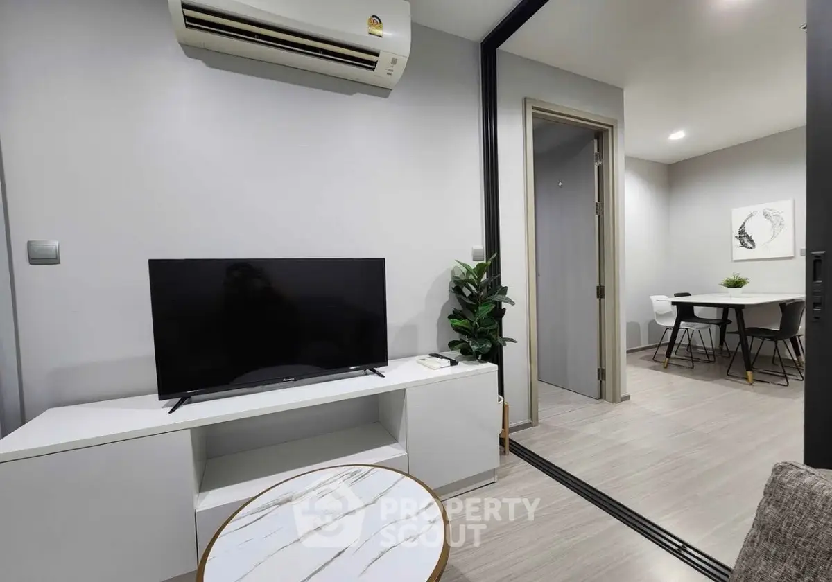 Modern living room with sleek TV setup and dining area in open layout apartment.