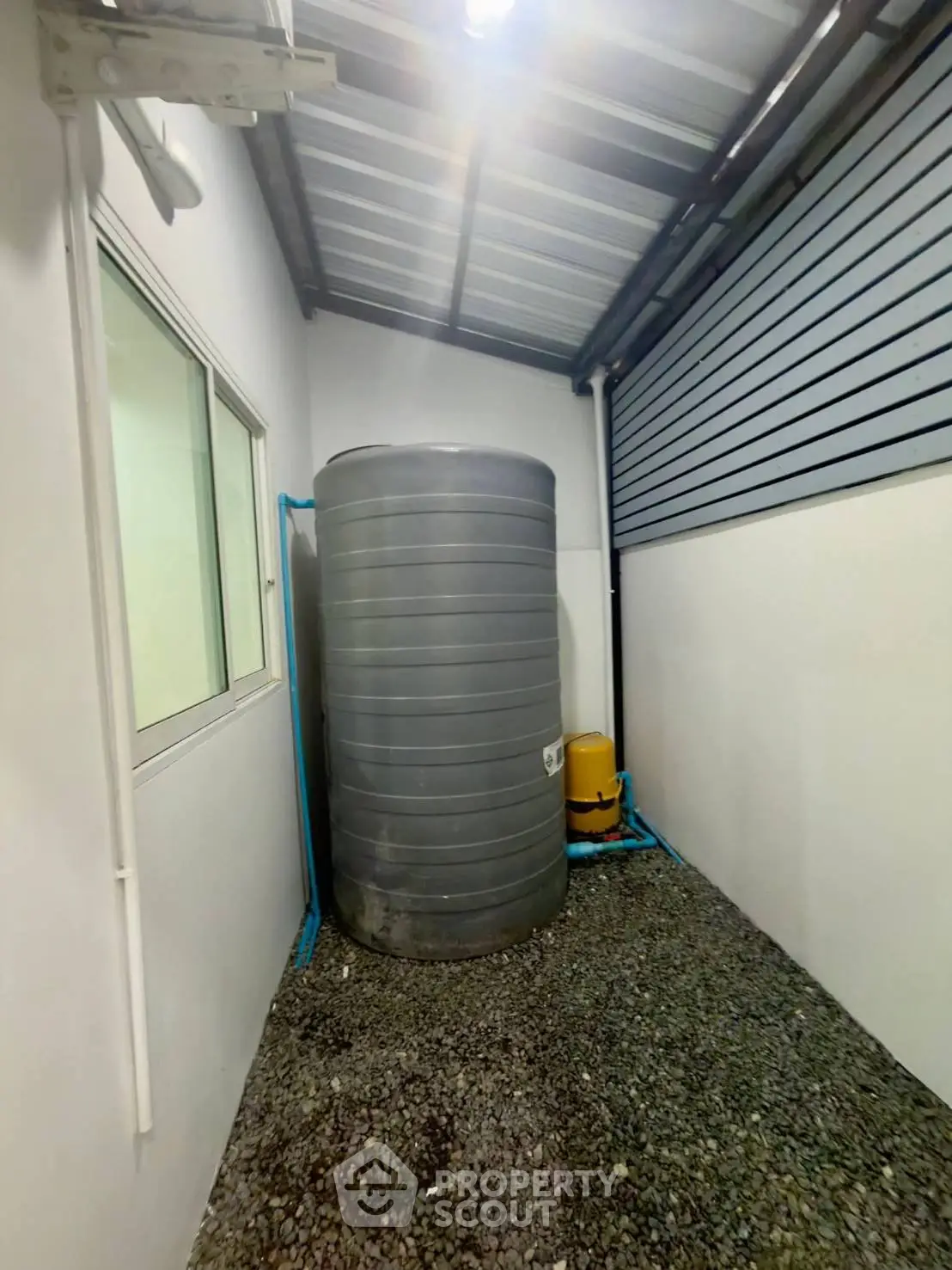 Outdoor utility area with water tank and gravel flooring