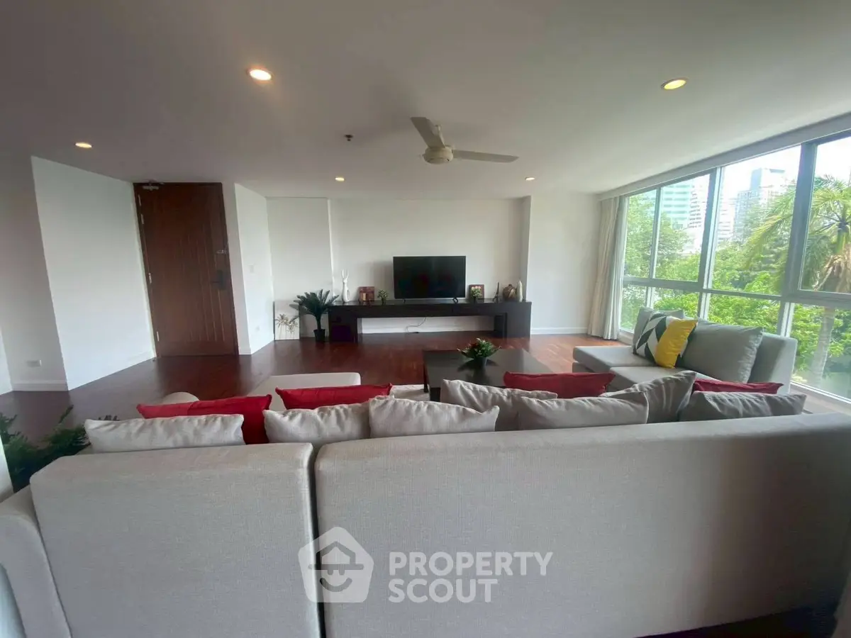 Spacious living room with modern decor and large windows offering a lush green view.