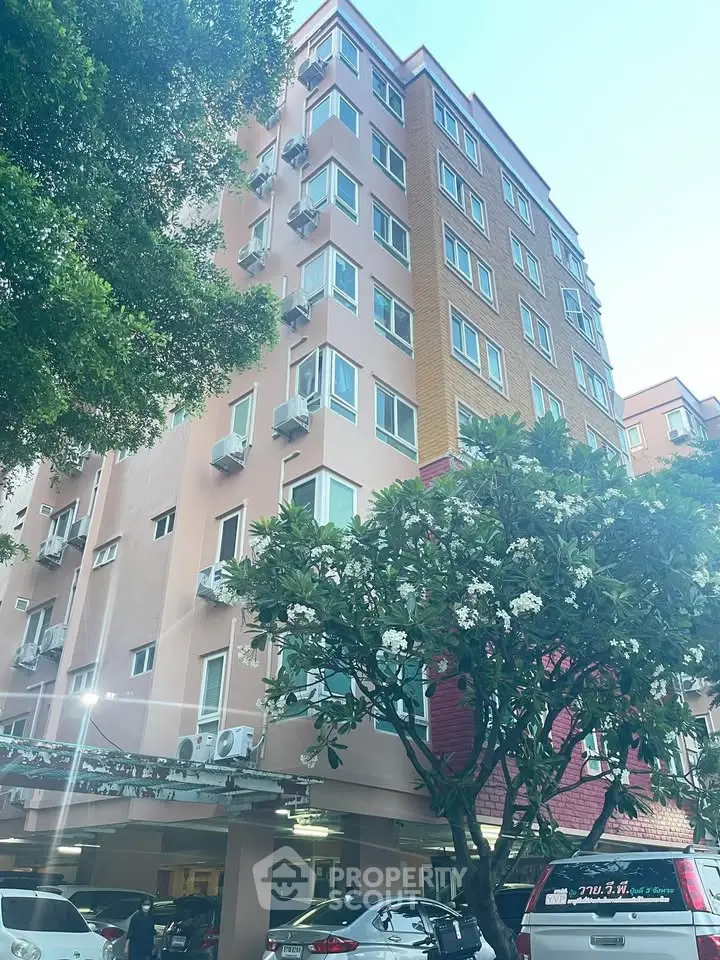 Charming multi-story residential building with lush greenery and ample parking space.