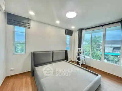 Spacious bedroom with large windows and modern bed frame, offering ample natural light and serene views.