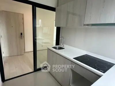 Modern kitchen with sleek cabinetry and electric cooktop in a compact apartment.