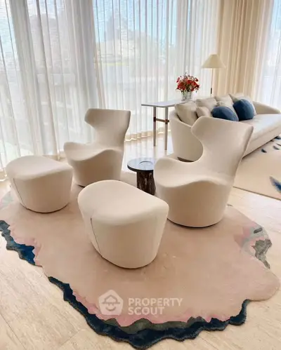 Elegant living room with modern chairs, plush rug, and natural light from large windows.