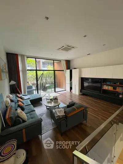 Spacious modern living room with large windows and garden view, featuring stylish furniture and wooden flooring.