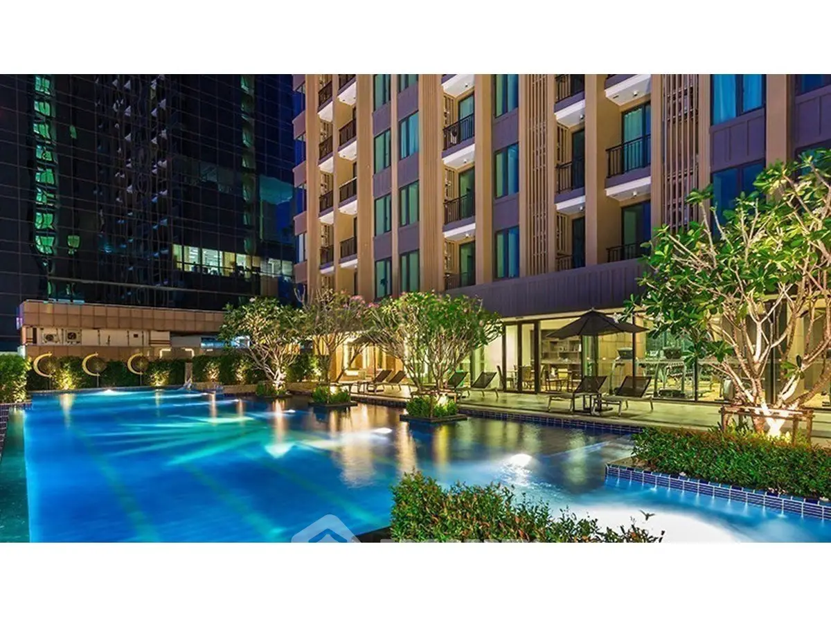 Luxurious apartment complex with stunning illuminated pool and lush greenery at night.