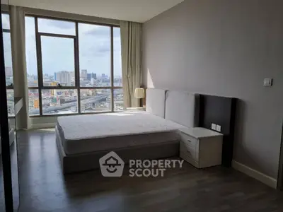 Spacious bedroom with large windows offering stunning city views in a modern apartment.