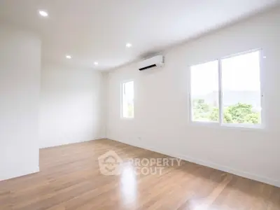 Spacious empty room with wooden flooring and large windows offering natural light and scenic views.