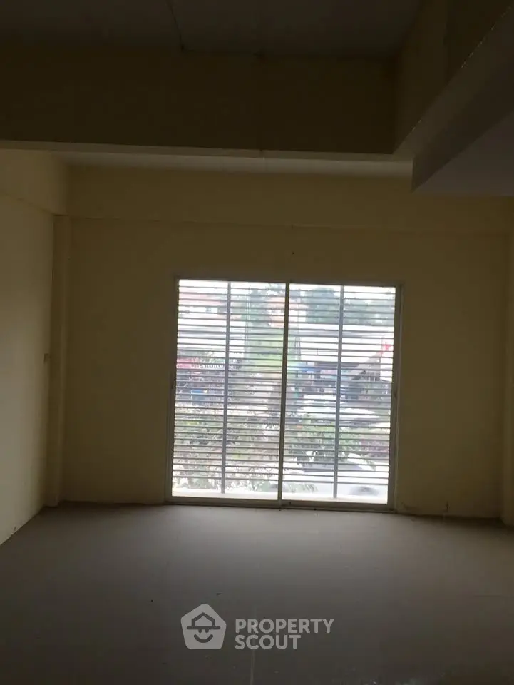Spacious room with large window offering natural light and urban view.