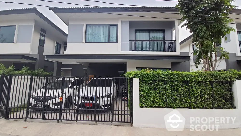 Modern two-story house with a sleek design, featuring a balcony, private parking, and a well-maintained hedge for privacy.