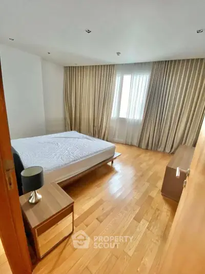 Spacious bedroom with wooden flooring and elegant curtains in modern apartment