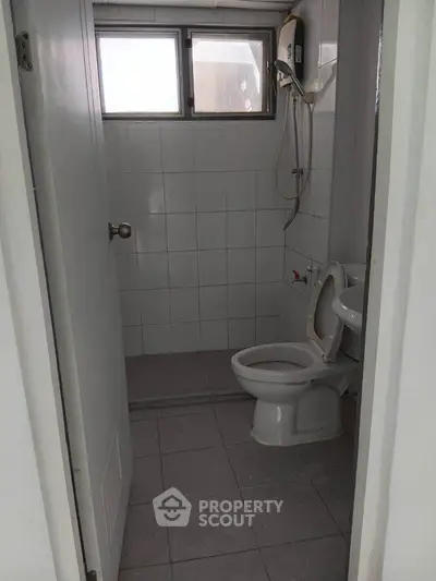 Compact bathroom with tiled walls and floor, featuring a toilet and shower area.