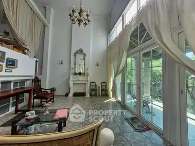 Elegant living room with high ceilings, chandelier, and large windows opening to a garden view.