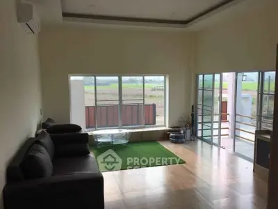 Spacious living room with large windows and countryside view, featuring modern furniture and wooden flooring.