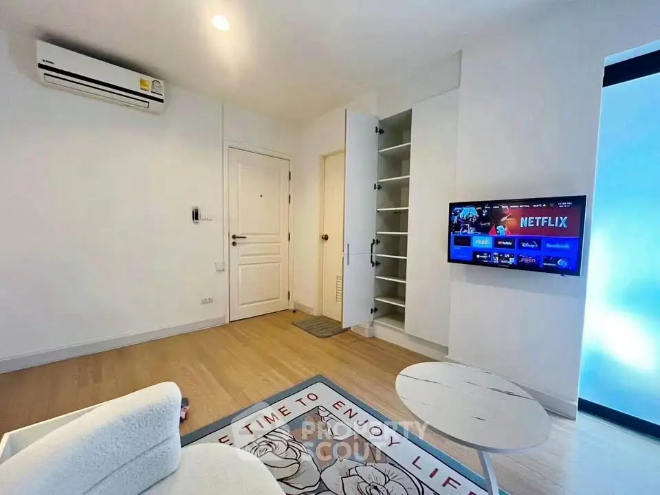 Modern living room with wall-mounted TV and open storage, featuring cozy seating and stylish decor.