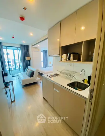 Modern studio apartment with open kitchen and cozy living area, featuring large windows and stylish decor.