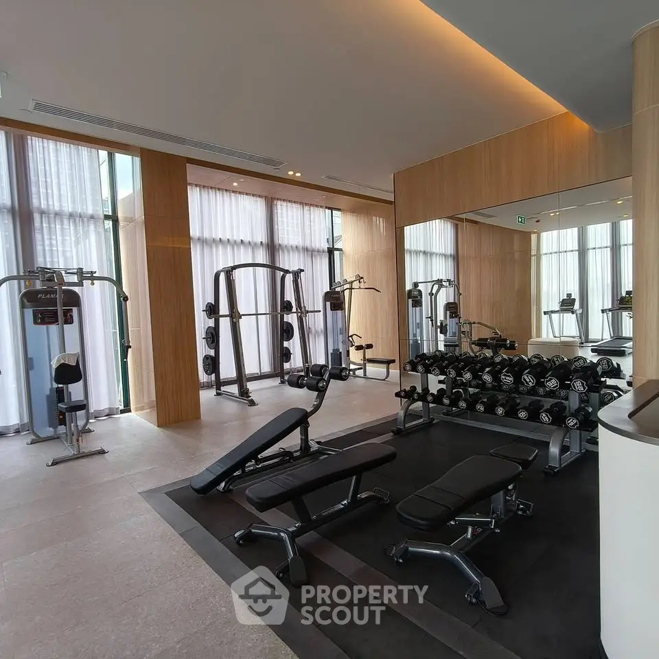 Modern gym with state-of-the-art equipment and floor-to-ceiling windows in luxury building.