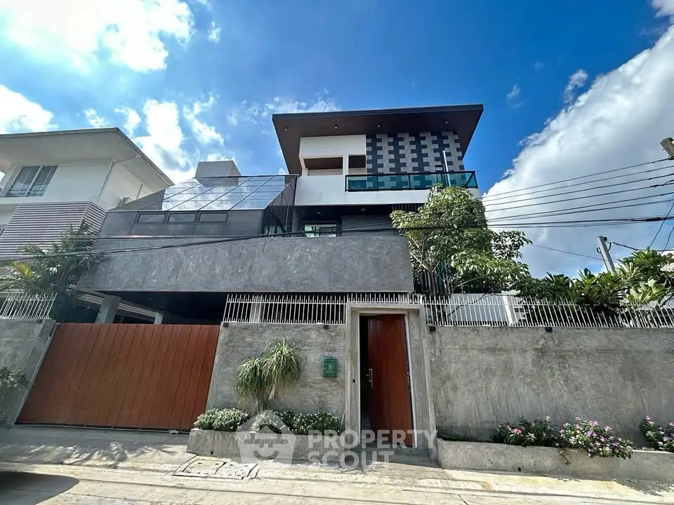 Modern three-story house with sleek design and lush greenery under a clear blue sky.