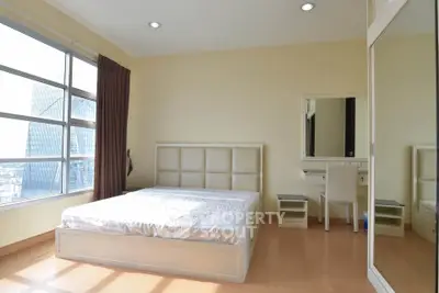 Spacious bedroom with large window and modern furnishings in high-rise apartment.